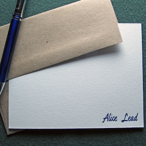 May include: A white card with a brown envelope on top of it. The card has the text "Alice Lead" printed in blue ink.