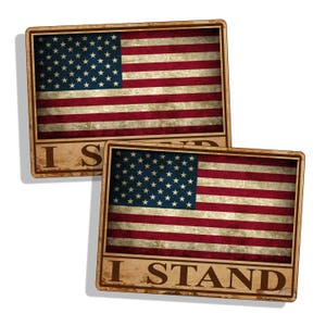 Puede incluir: Dos pegatinas de aspecto de madera desgastada con una bandera estadounidense y el texto "I Stand".