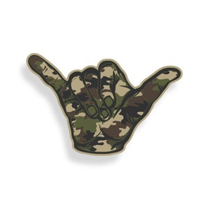 May include: A green and brown camouflage pattern hand sign, shaped like a 'hang loose' gesture, with the index finger and pinky finger extended.