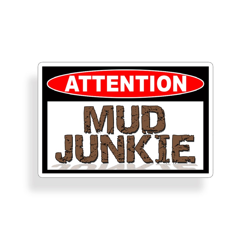 May include: A white sign with black and red borders. The sign reads "ATTENTION" in a red oval and "MUD JUNKIE" in brown letters.
