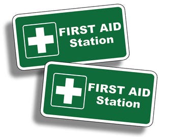 Pode incluir: Dois sinais retangulares verdes com bordas brancas. Cada sinal tem um símbolo de cruz branca e o texto "FIRST AID Station".
