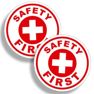 May include: Two white round stickers with a red border. The stickers have a red cross in the center and the words "SAFETY FIRST" in a red circle around the cross.