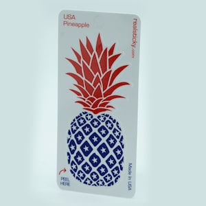 May include: A red and blue pineapple sticker with a white background. The pineapple is decorated with white stars on a blue background. The sticker says "USA Pineapple" and "realsticky.com". It also says "Made in USA" and "Peel Here" with an arrow.