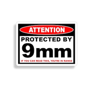 Op de afbeelding: Een zwart-wit waarschuwingsbord met rode tekst die "ATTENTION" en "PROTECTED BY 9mm" luidt. Het bord bevat ook de tekst "IF YOU CAN READ THIS, YOU'RE IN RANGE".