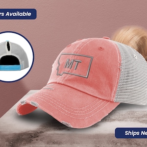 May include: A pink and gray distressed baseball cap with a mesh back and a ponytail hole. The cap has a gray embroidered patch with the state outline of Montana and the letters "MT".