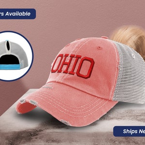 May include: A coral-colored distressed baseball cap with the word "OHIO" embroidered in red. The cap features a mesh back and a ponytail opening. The image also shows a close-up of the back of the cap and the text "14 Colors Available".