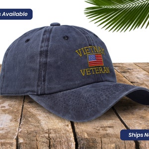 May include: A dark blue baseball cap with an embroidered American flag and the text "VIETNAM VETERAN" in gold thread.
