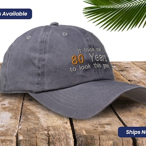 May include: A gray baseball cap with the text "It took me 80 Years to look this good" embroidered in white and orange.