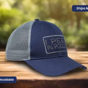 May include: A blue and gray trucker hat with a white mesh back. The hat has a white patch with the text "I PEE IN POOLS" in gray.