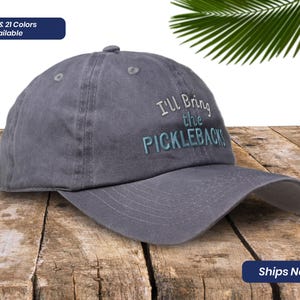 May include: A gray cotton baseball cap with the text "I'll Bring the Picklebacks" embroidered in blue and white.