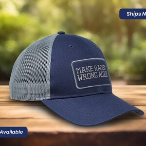 May include: A navy blue and gray trucker hat with a white mesh back. The hat has a gray patch with the text "MAKE RACISM WRONG AGAIN" in white.