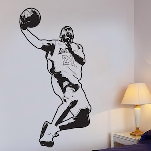 May include: Black and white silhouette of a basketball player in mid-air, wearing a jersey with the text "LAKERS 24" on the front. The player is holding a basketball in their right hand.