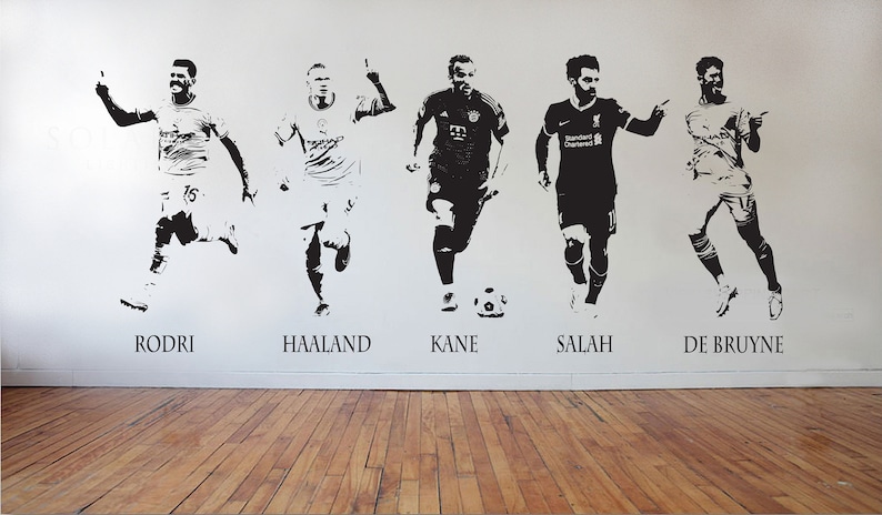 May include: Black and white wall decals featuring five soccer players in action poses. Each player is labeled with their name: Rodri, Haaland, Kane, Salah, and De Bruyne. The decals are applied to a white wall above a wooden floor.