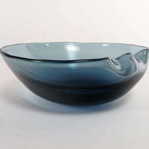May include: A handcrafted, blue glass bowl with a unique, wavy rim. The bowl transitions from a deep navy at the base to a lighter, sky blue towards the top. This decorative piece is ideal for serving or display.