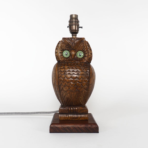Peut inclure: Lampe en bois en forme de hibou avec des yeux verts. La lampe présente des détails sculptés et une finition marron foncé. La lampe en forme de hibou repose sur une base carrée en bois et possède une douille.