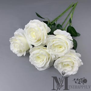 Puede incluir: Un ramo de seis rosas blancas con tallos y hojas verdes. Las rosas están en plena floración, con múltiples capas de pétalos. El fondo es de color gris liso. El logotipo "MINIHAPPYL" está en la parte inferior.