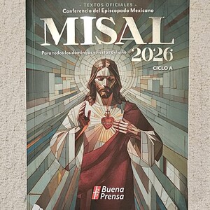 May include: A hardcover book titled "MISAL 2026" with the text "Para todos los domingos y fiestas del año" and "CICLO A". The cover features an illustration of Jesus with a heart and a stained glass background. The publisher's logo "Buena Prensa" is at the bottom.