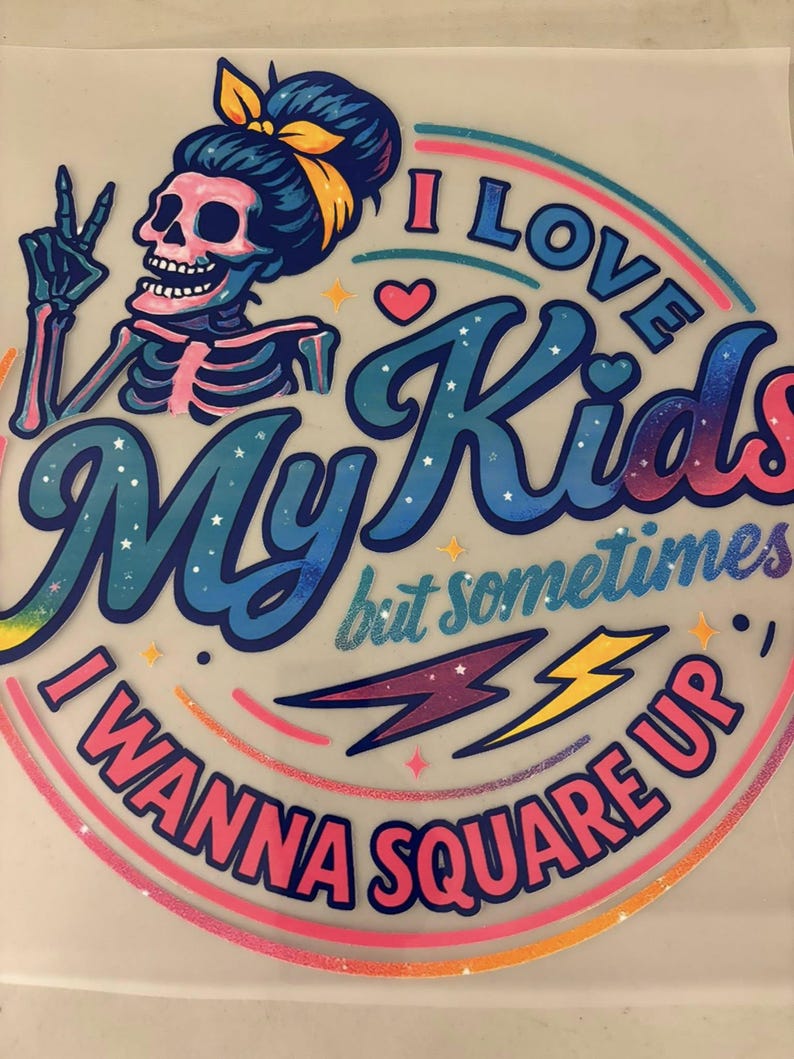 May include: A vibrant graphic with the text "I Love My Kids but sometimes I Wanna Square Up." The design includes a skeleton with a blue bun and yellow bow, a peace sign, and a rainbow arc. Pink, blue, and yellow lightning bolts are also included.