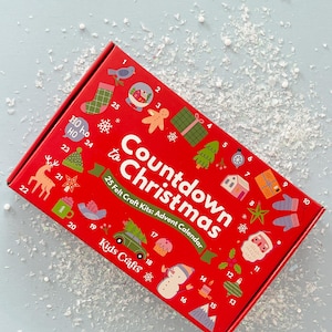 Puede incluir: Caja roja con una cuenta atrás hasta Navidad. La caja contiene 25 kits de manualidades de fieltro para un calendario de adviento. El texto de la caja dice "Countdown to Christmas" y "25 Felt Craft Kits: Advent Calendar". La caja está decorada con ilustraciones festivas y números.