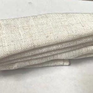 May include: A folded strip of off-white, textured fabric with a visible woven pattern. The material has a natural, light beige appearance with subtle flecks throughout the weave, showing a consistent, dense, and durable textile construction.