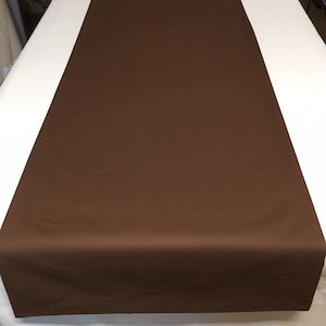 May include: A brown table runner made of fabric. The runner is flat and smooth with a subtle sheen.