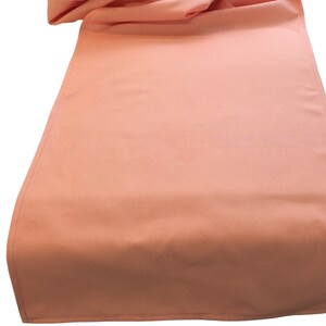 May include: A peach colored table runner. The runner is made of a smooth fabric and has a subtle sheen.