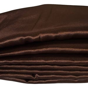 May include: A folded stack of brown satin fabric. The fabric has a smooth, shiny surface with visible folds and creases. The color is a rich, dark brown, and the fabric appears to be soft and flowing. The image is well-lit, highlighting the texture and sheen of the material.