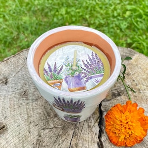 Puede incluir: Una taza de cerámica blanca con un asa negra y el texto "But First, Coffee" en negrita negra. La taza se encuentra sobre un fondo borroso, sugiriendo un ambiente acogedor.