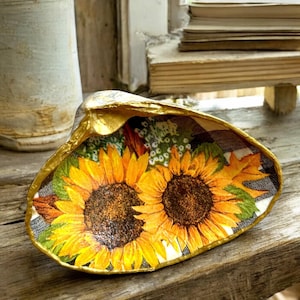 May include: A decorative seashell dish with a gold rim and a floral design featuring sunflowers and plaid accents.