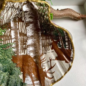 Puede incluir: Una concha decorativa con un borde dorado, que representa una escena de bosque con árboles, ciervos y un fondo blanco.