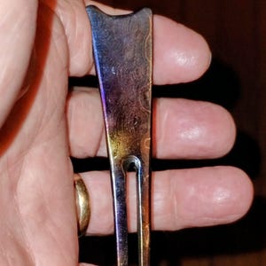 May include: A multi-colored golf divot repair tool. The tool has a textured, patterned surface with hues of blue, purple, and gold. The tool has a forked end for repairing divots and a curved top.