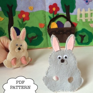 May include: Two felt finger puppets of bunnies. One bunny is light brown with pink ears and the other is gray with pink ears. Both bunnies have black eyes and noses. The bunnies are sitting on a white surface. The text "PDF PATTERN" is written in a white cloud on a blue background.