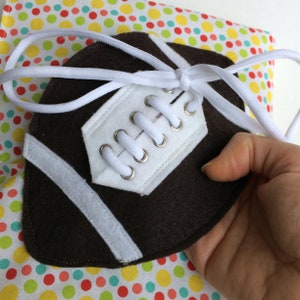 Puede incluir: Un balón de fútbol de fieltro marrón y blanco con cordones blancos y una cuerda blanca atada alrededor.