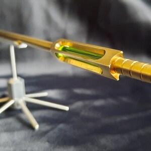 May include: A gold-coloured metal rod with a green glass section and a green tip, mounted on a silver metal stand.