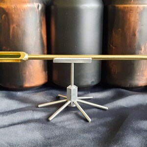May include: A gold-coloured arrow with a green glass section and a pointed tip, displayed on a silver metal stand with multiple arms.