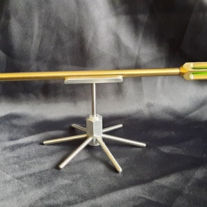 May include: A gold-coloured arrow with a green glass insert is displayed on a silver metal stand with six legs.