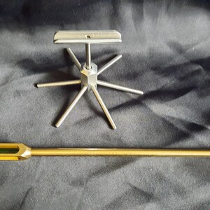 May include: A gold-coloured metal rod with a green glass section and a pointed tip, and a silver metal stand with six arms extending outwards from a central hub.