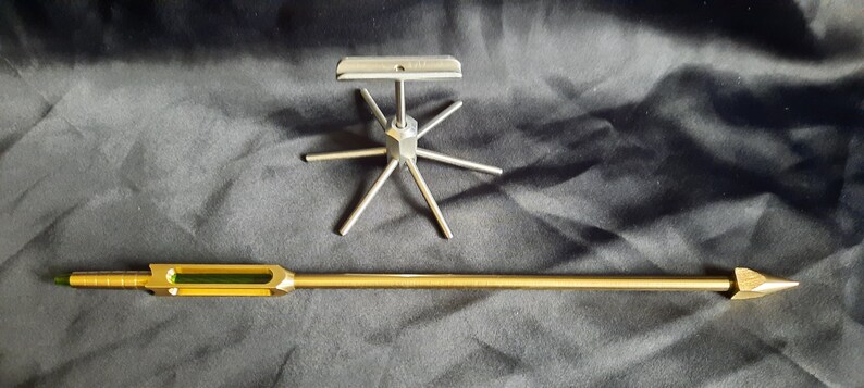 May include: A gold-coloured metal rod with a green glass section and a pointed tip, and a silver metal stand with six arms extending outwards from a central hub.