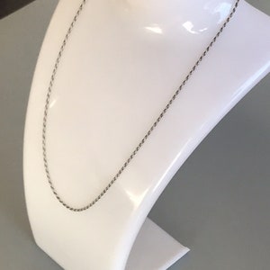 May include: A silver rope chain necklace on a white display stand.
