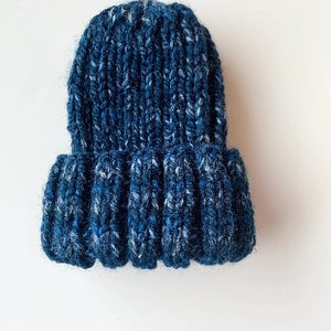May include: A blue knitted beanie with a textured pattern. The beanie is made of a soft, fuzzy yarn.