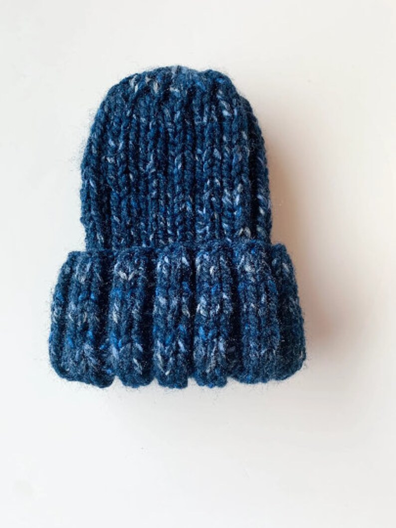 May include: A blue knitted beanie with a textured pattern. The beanie is made of a soft, fuzzy yarn.