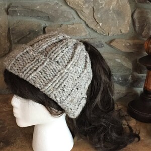 May include: A gray knitted beanie with a ponytail hole. The beanie is made of a soft, textured yarn and has a slouchy fit.