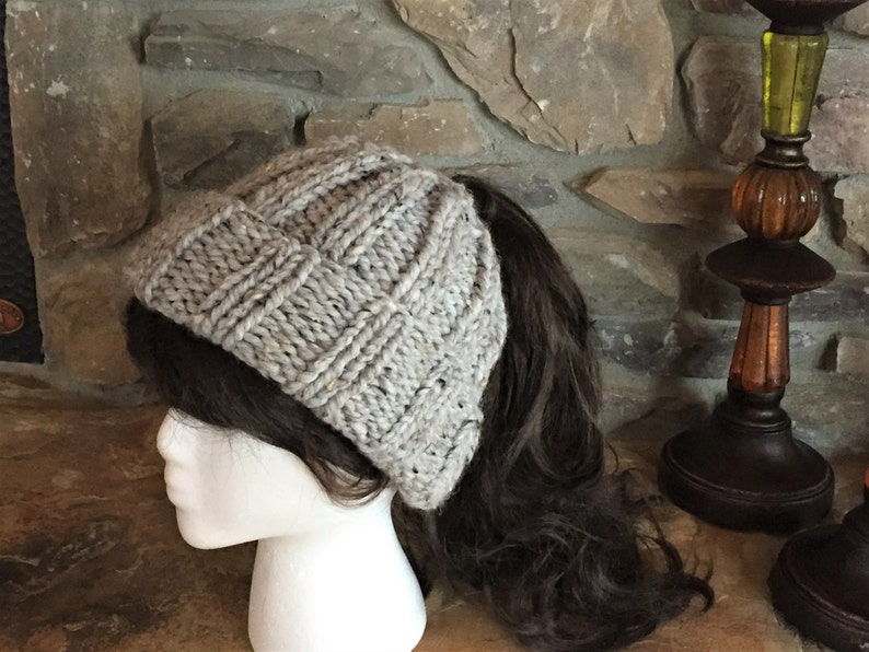 May include: A gray knitted beanie with a ponytail hole. The beanie is made of a soft, textured yarn and has a slouchy fit.