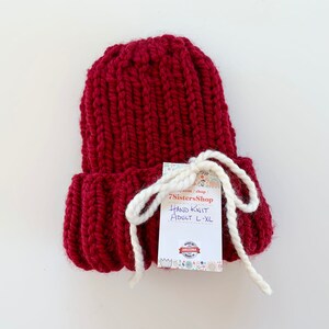 May include: A hand-knitted burgundy beanie with a white tag that reads "7SistersShop Hand Knit Adult L-XL".