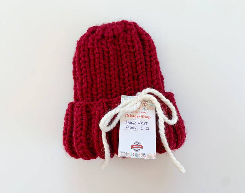May include: A hand-knitted burgundy beanie with a white tag that reads "7SistersShop Hand Knit Adult L-XL".