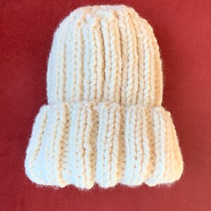 May include: A white knitted beanie hat with a ribbed texture. The hat is folded down at the brim.