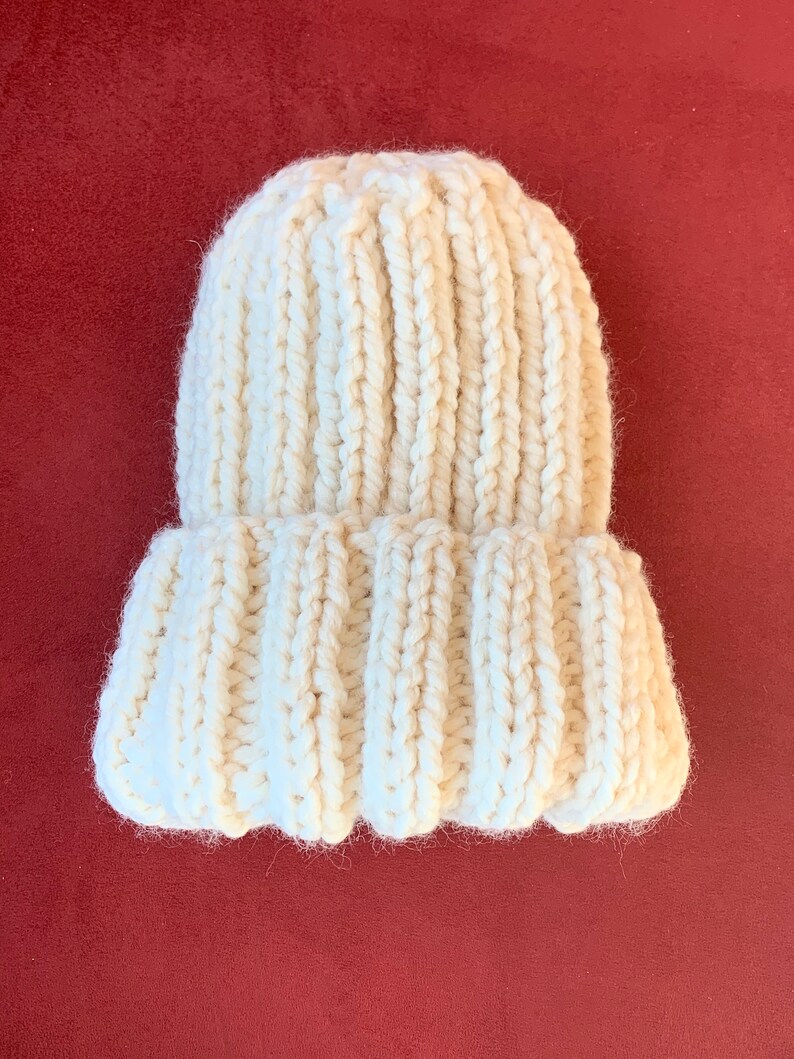 May include: A white knitted beanie hat with a ribbed texture. The hat is folded down at the brim.