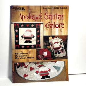 May include: A craft leaflet titled "Appliqué Santas Galore" featuring various Christmas-themed appliqué projects. The cover displays images of Santa Claus designs on a wall hanging, a sack, and a tree skirt. The leaflet is by Jean Wells.