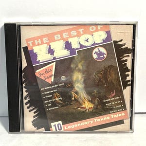May include: A CD case featuring "The Best of ZZ Top." The cover art depicts a campfire scene with cowboys and horses, with text that reads "10 Legendary Texas Tales." The case is in a clear plastic sleeve.