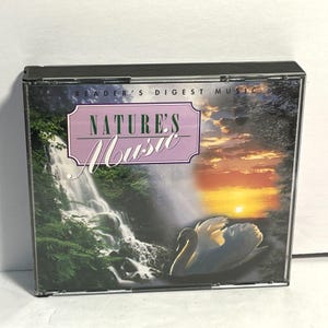 以下が含まれることがあります： Nature's MusicというタイトルのReader's Digest MusicのCDケース。カバーには、暗い池で泳ぐ白い白鳥、緑の葉に囲まれた滝、そして背景に鮮やかなオレンジと黄色の夕焼けが描かれています。